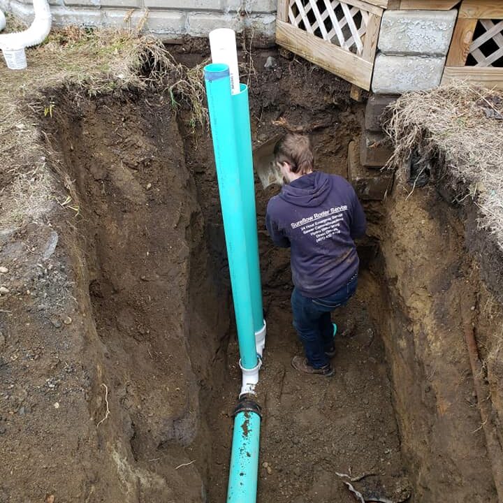 A man is standing in the dirt near pipes.